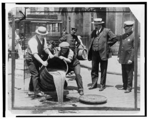 Photograph from 1921 showing men pouring alcohol down the sewer under the watch of police